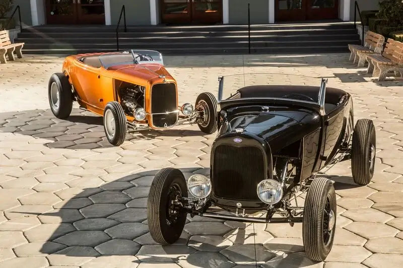 Two vintage hot rod roadsters parked on a paved courtyard